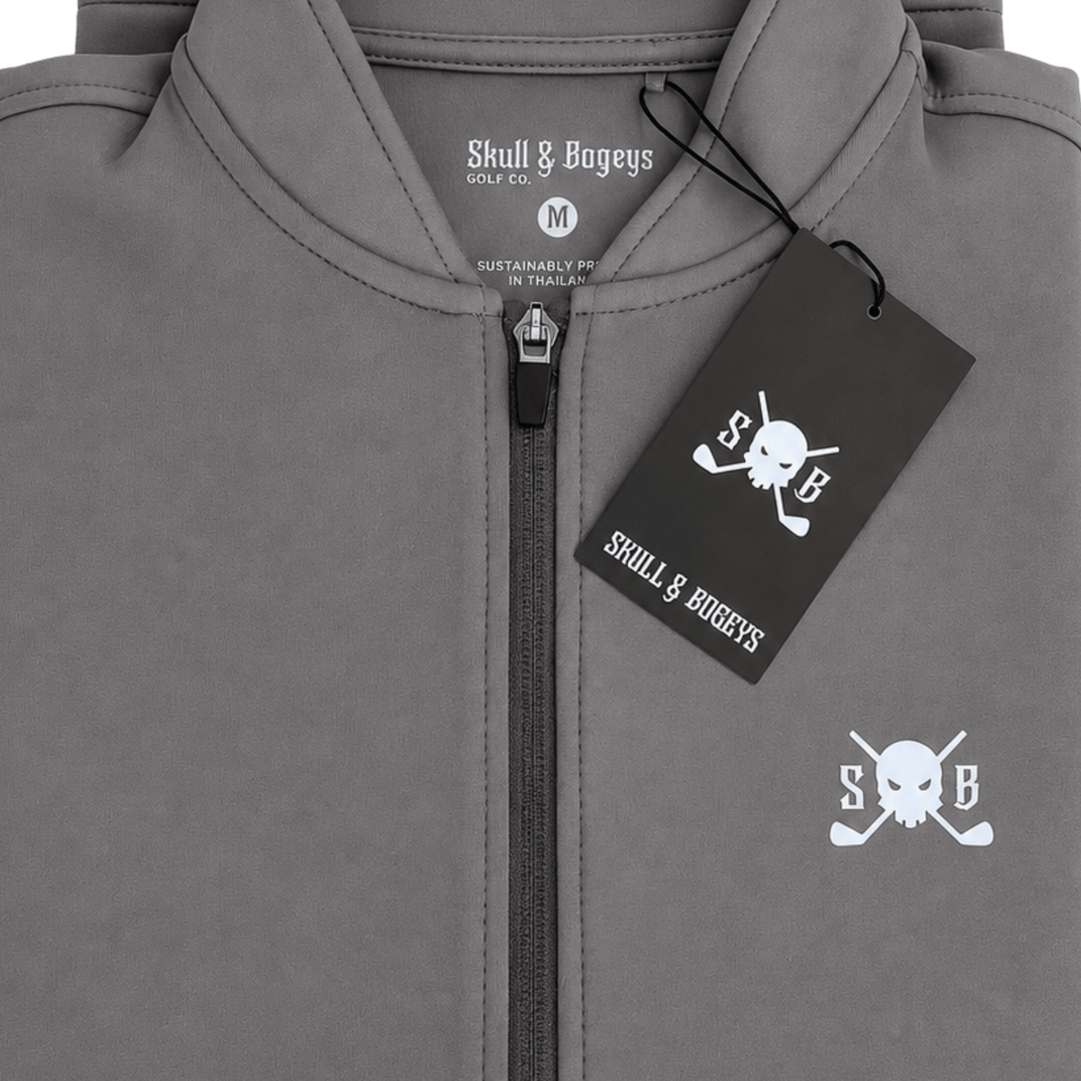 Close-up of a gray zip-up hoodie with a black hangtag and white printed Skull & Bageys branding, including a skull-and-crossbones logo on the chest.