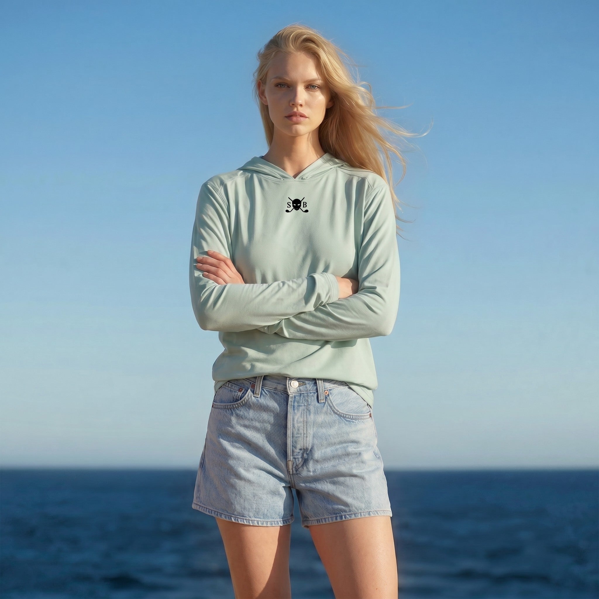 Woman wearing a light blue hoodie and denim shorts standing against a clear blue sky.