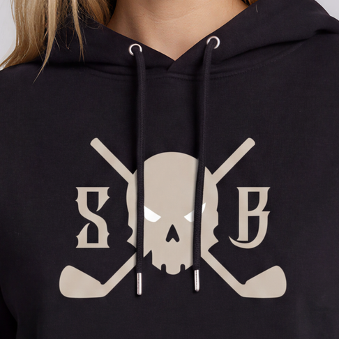 A woman modeling a black cropped hoodie with a beige graphic on the front featuring crossed hockey sticks and the letters 'S' and 'B' around a central symbol. She is wearing dark gray jeans against a solid light gray background.