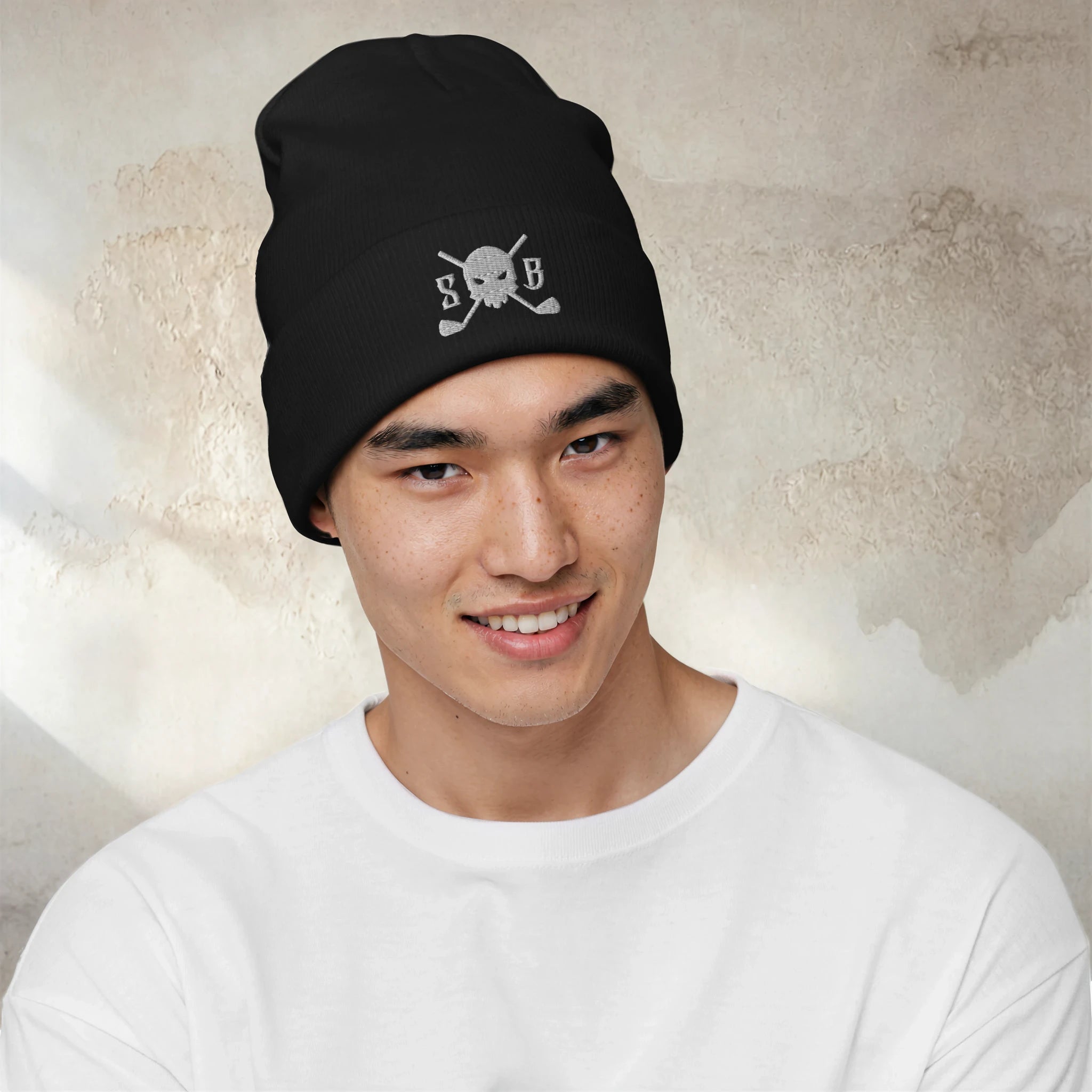Person wearing a black beanie with a logo against a textured wall background