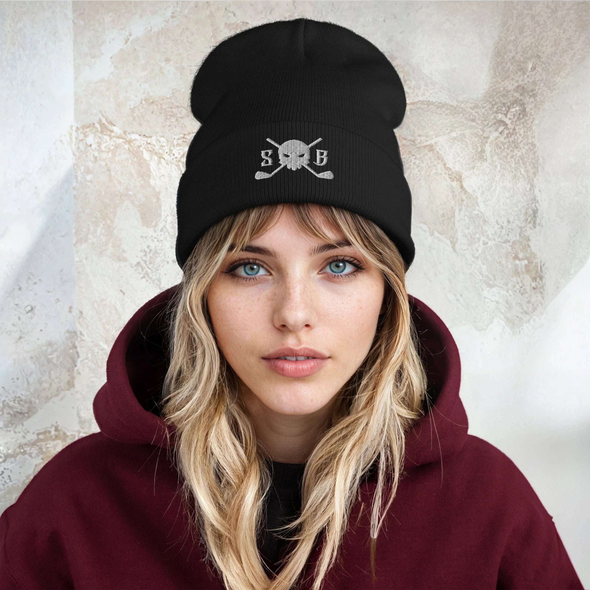 Person wearing a black beanie with a skull and crossbones design on a textured wall background