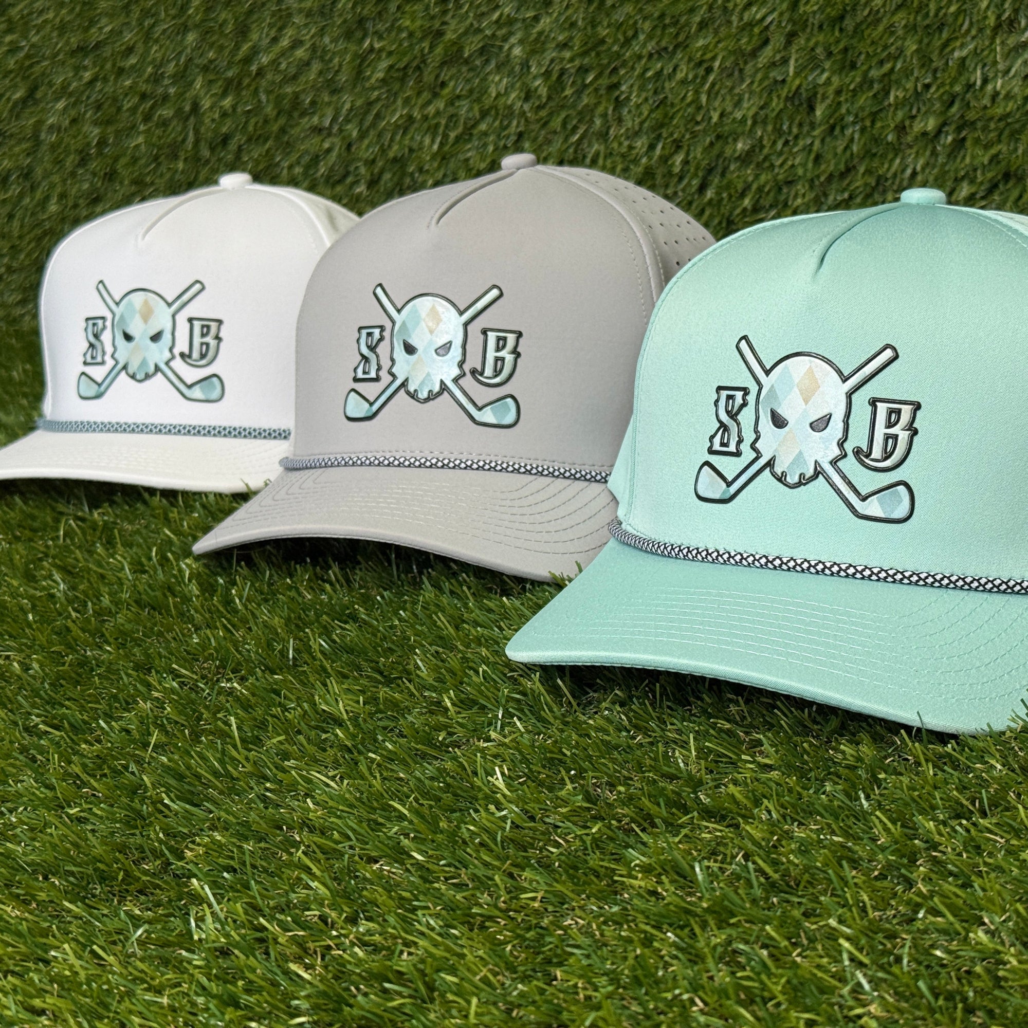 Three baseball caps with a skull and crossbones logo on a grass background