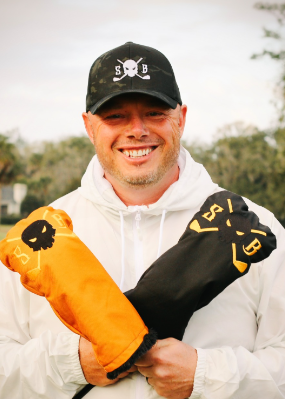 Man holding orange and black items with a logo in a golf course setting