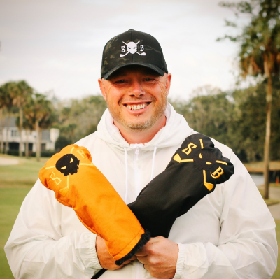 Man holding orange and black items with a logo in a golf course setting