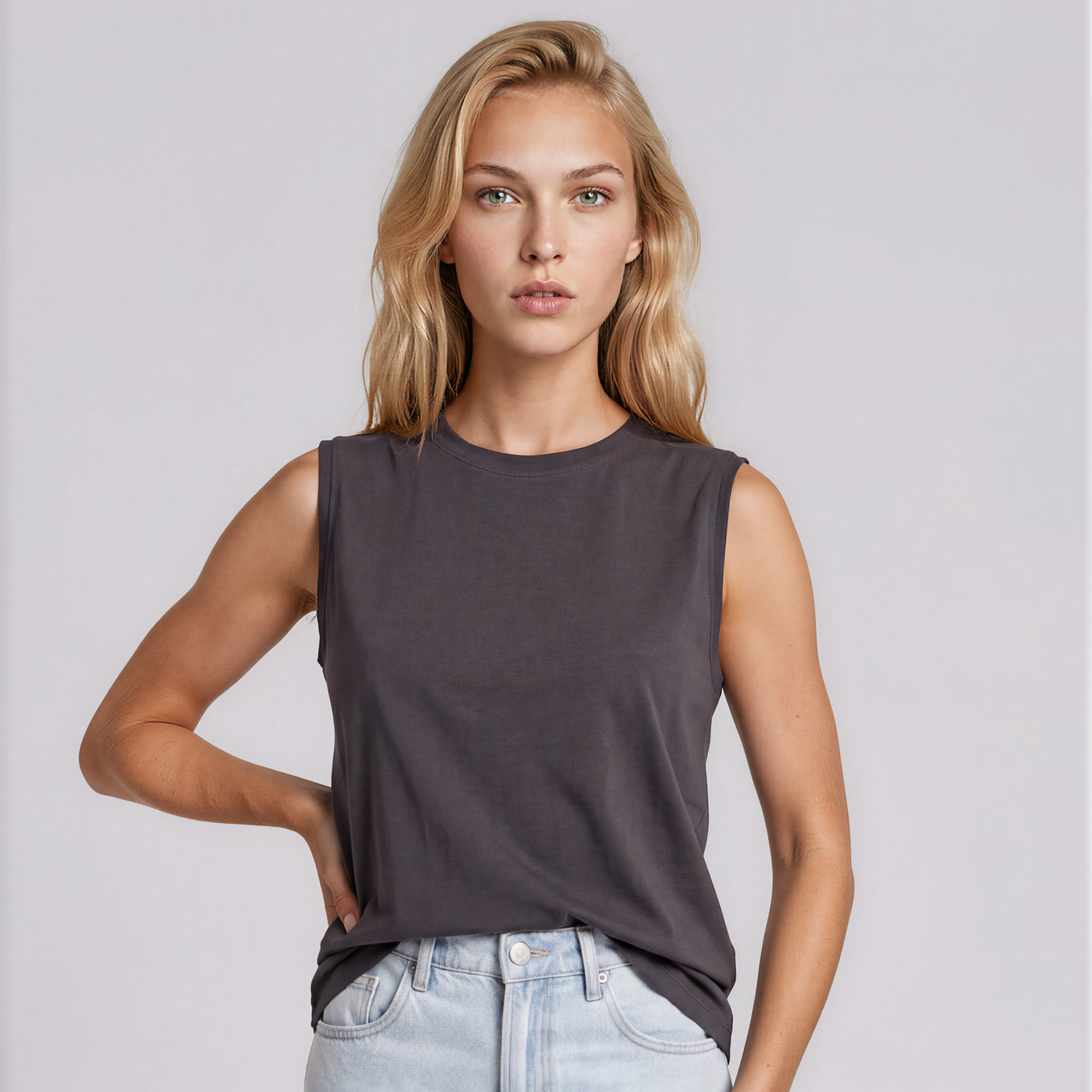 A blonde model wearing a dark charcoal gray sleeveless crewneck top and light wash blue jeans, standing against a light gray studio background. A small 'AI Generated | BOTIKA' watermark is visible in the bottom right corner.