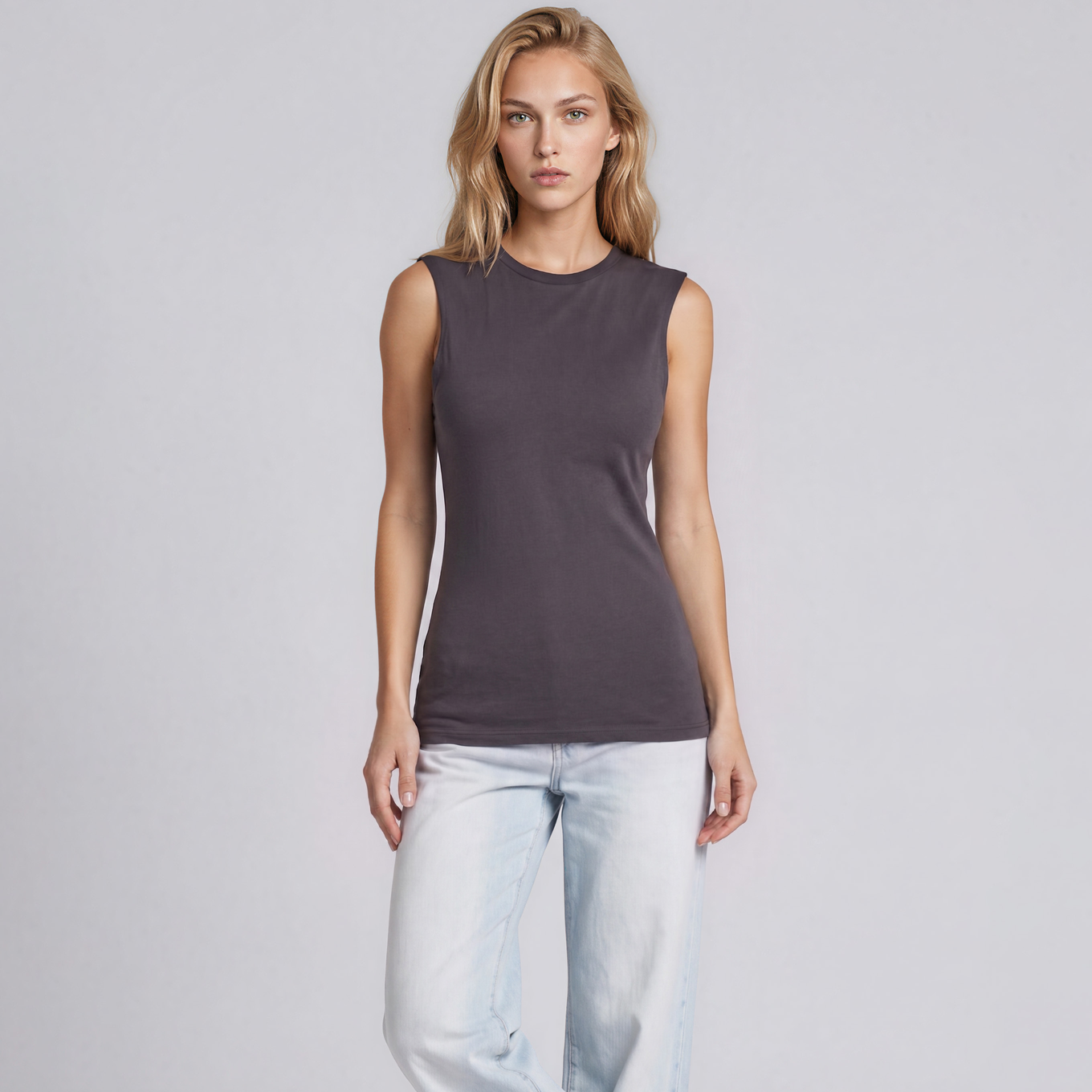A woman modeling a sleeveless dark gray crewneck top, paired with light-wash wide-leg jeans and white sneakers, against a light gray studio background.