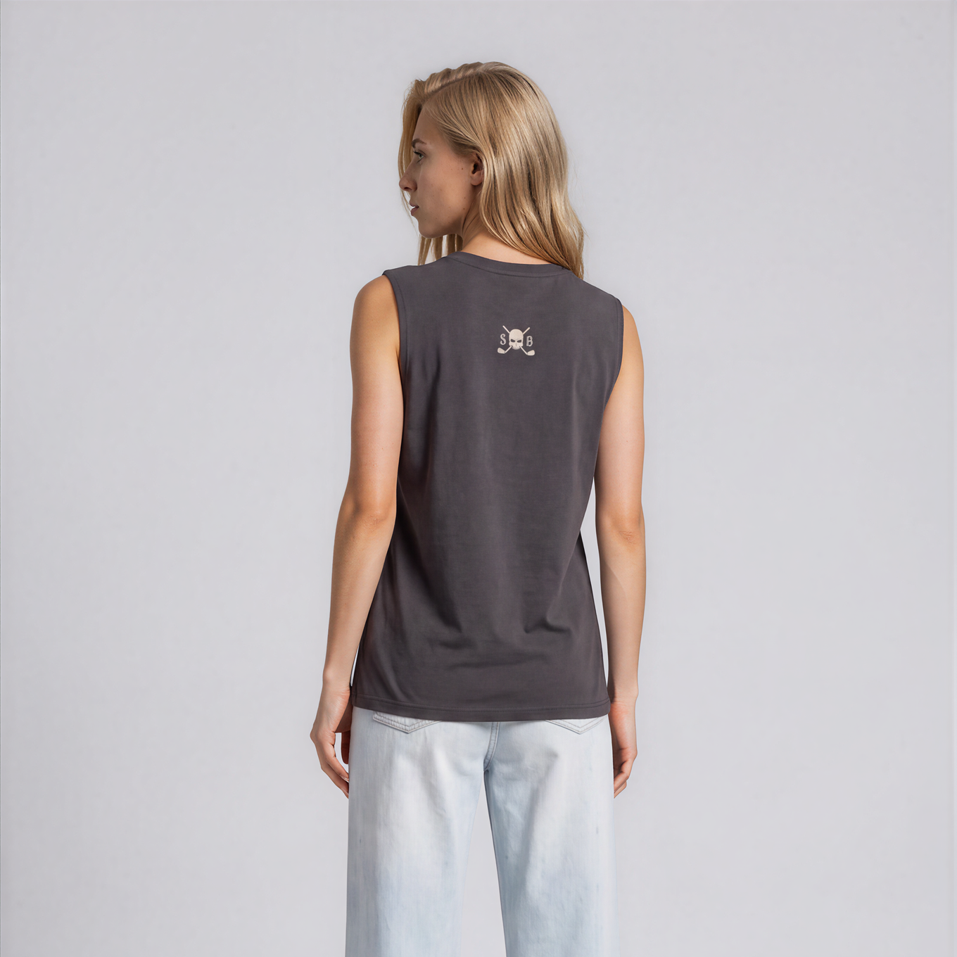 A woman shown from the back wearing a dark gray sleeveless top with a small graphic on the upper back and light-wash wide-leg jeans, standing against a light gray studio background.
