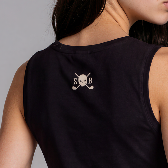 A woman shown from the back wearing a black sleeveless crop top with a small skull-and-crossbones graphic on the upper back, paired with light-wash denim shorts, against a plain gray studio background.