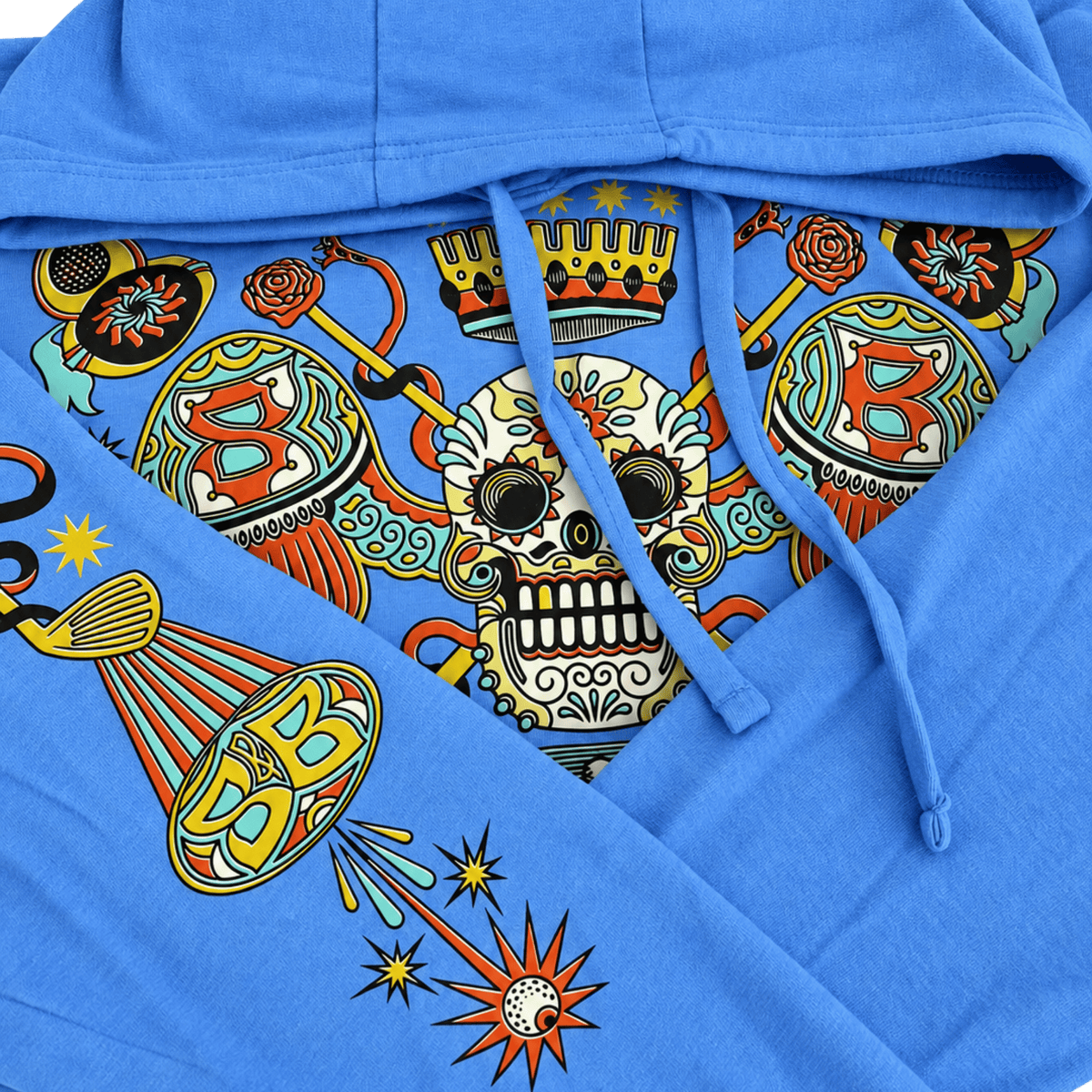 A close-up of a bright blue hoodie featuring a colorful graphic print on the inner hood lining and drawstrings. The print includes a central sugar skull with a crown, decorative globes, and starburst motifs in yellow, orange, red, black, and white.