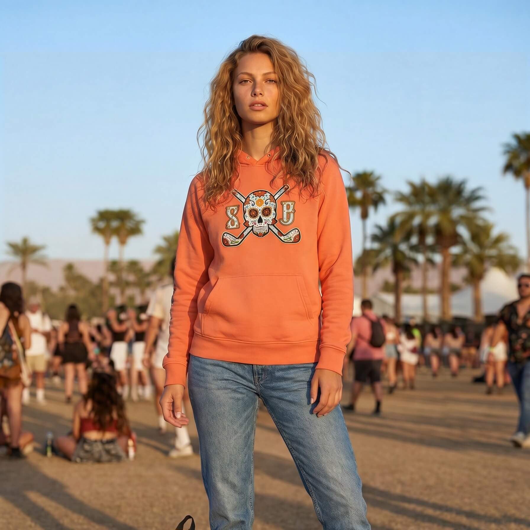 Woman wearing an orange sweatshirt with a skull design and blue jeans, standing outdoors with palm trees and people in the background.