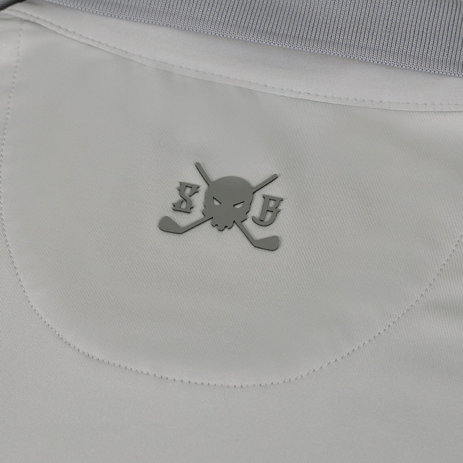 Close-up of a Skull & Bogeys Golf Co. gray fabric garment with a curved seam and a small gray skull-and-crossed-golf-club logo centered on the chest.