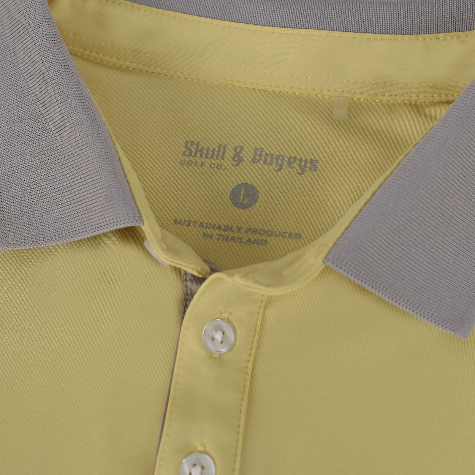 Close-up of a Skull & Bogeys Golf Co. polo shirt collar and upper placket showing a pale yellow body, light gray ribbed collar, and visible neck label reading Skull & Bogeys Golf Co.