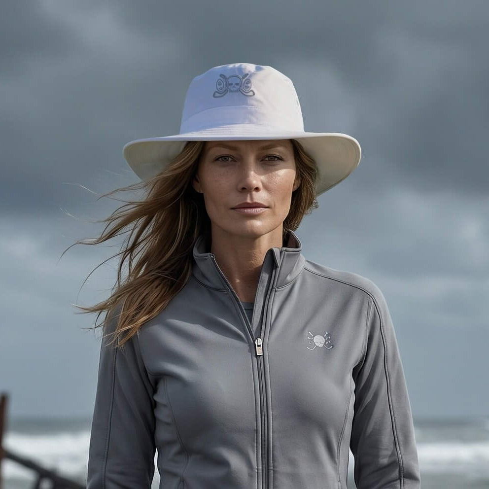 Woman in gray jacket and white pants standing on a beach with a shipwreck in the background