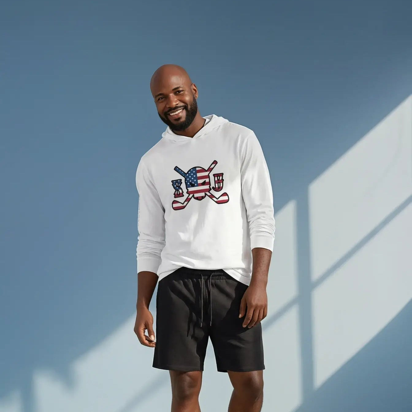 Man wearing a white sweatshirt with a graphic design and black shorts standing against a blue wall.