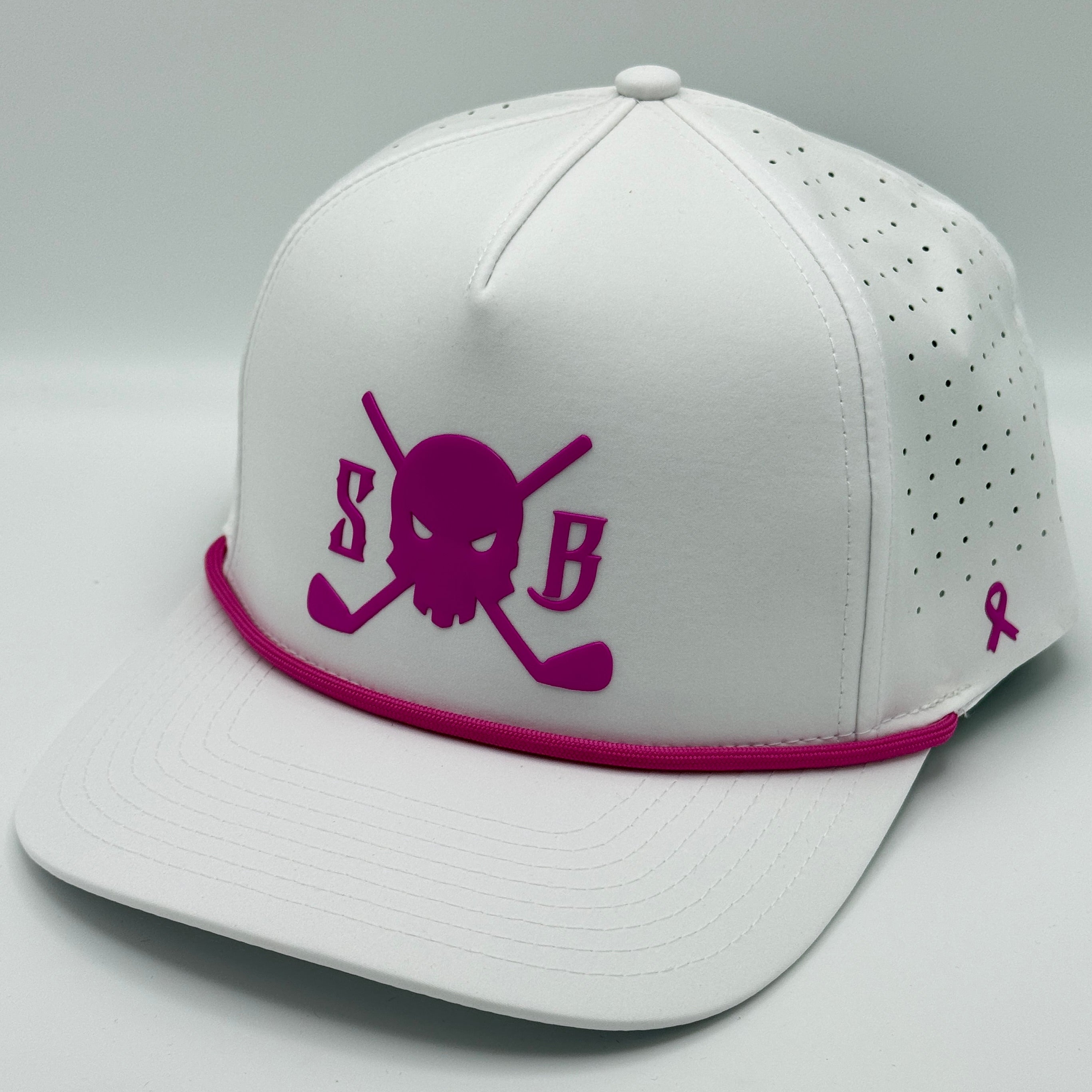 A white structured baseball cap with a bright pink/magenta logo on the front featuring a skull and crossed golf clubs with the letters 'S' and 'B'. The brim has a matching pink band, and the side panels have perforated holes with a small pink ribbon logo on the back.