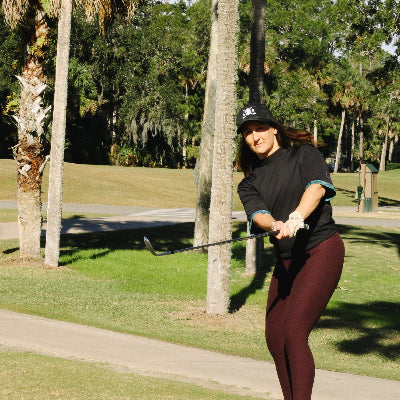 Woman playing golf on a grassy course with palm trees in the background