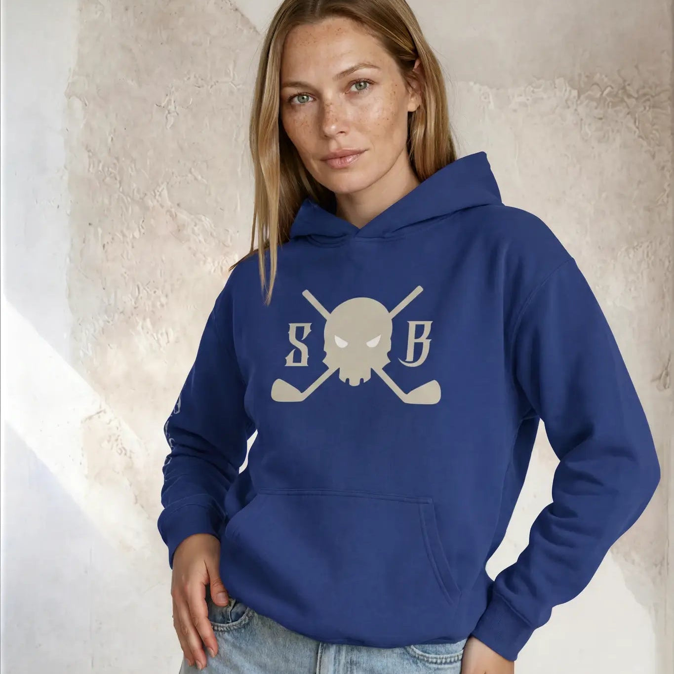 Woman wearing a blue hoodie with a logo against a textured wall.