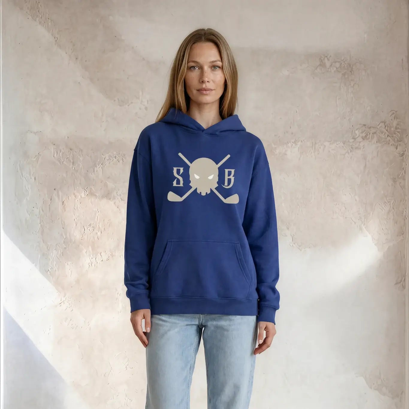Person wearing a blue hoodie with a logo, light blue jeans, and white sneakers against a neutral background