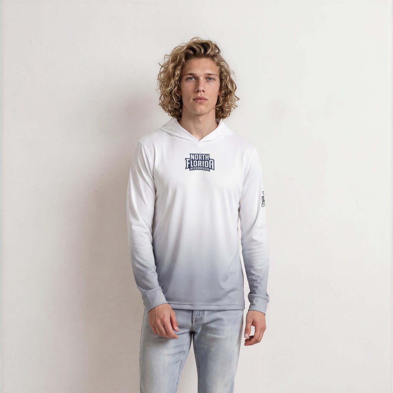 Person wearing a white hoodie with a logo and light blue jeans against a plain background