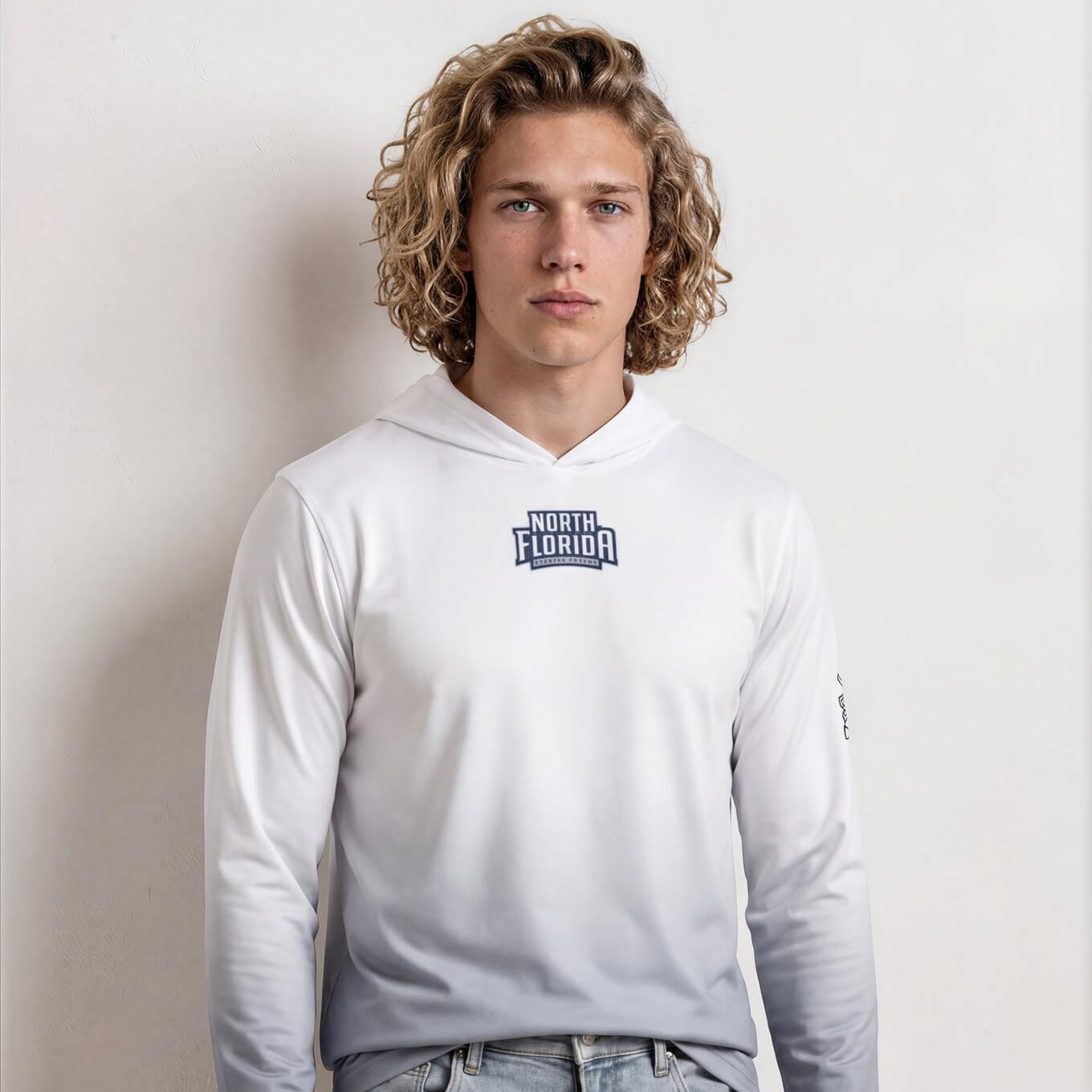 Person wearing a white hoodie with a logo and light blue jeans against a plain background