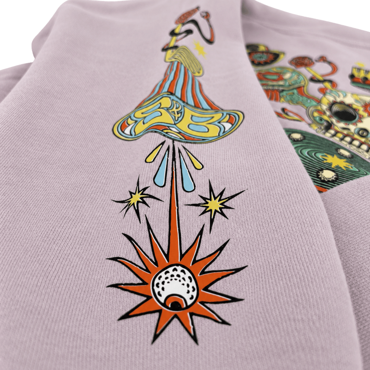 A close-up of a light lavender sweatshirt featuring a colorful psychedelic graphic of a mushroom cloud launching a rocket, with stars and a rocket tail burst below. A second graphic is partially visible on the right side.