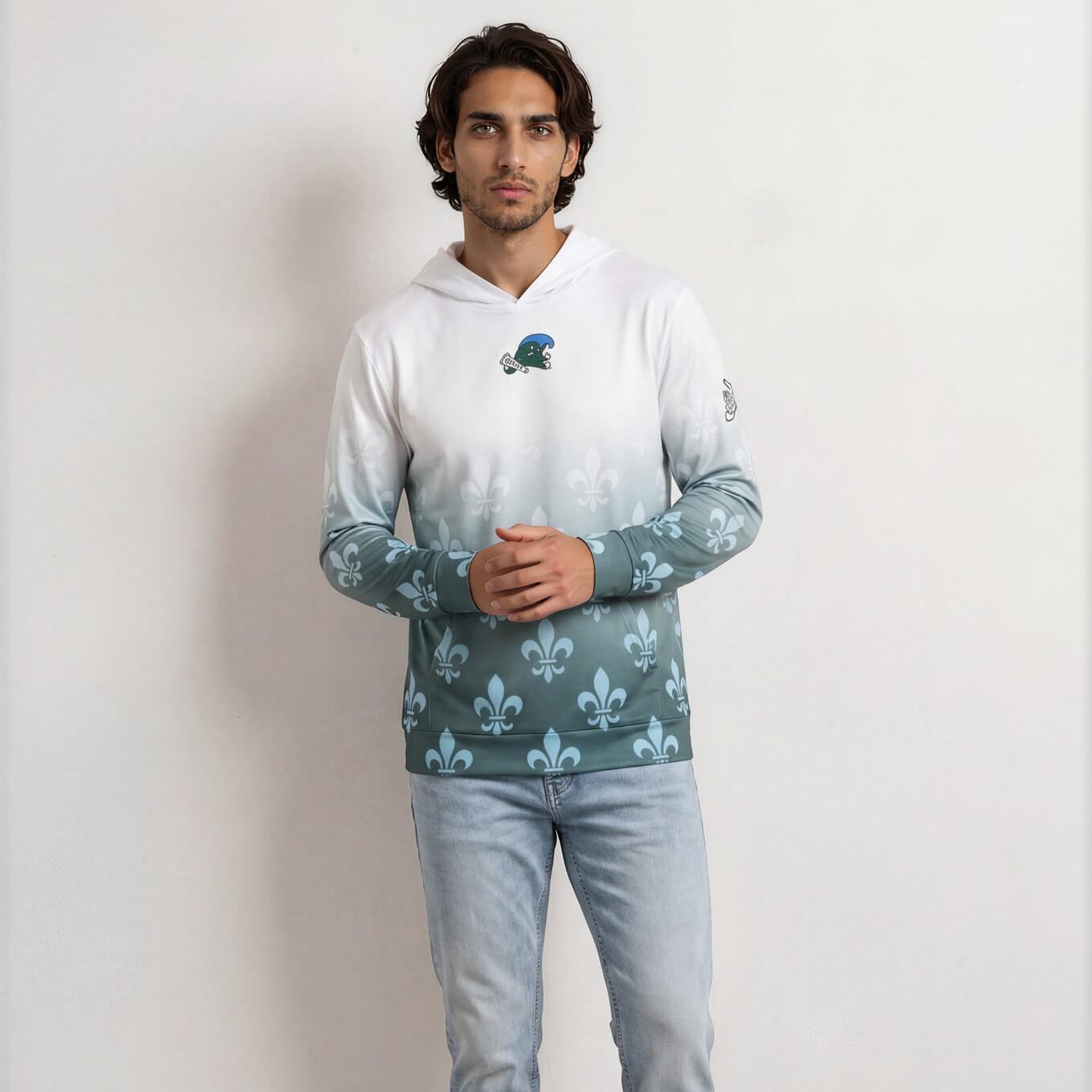 Man wearing a white hoodie with a graphic design and light blue jeans on a plain background