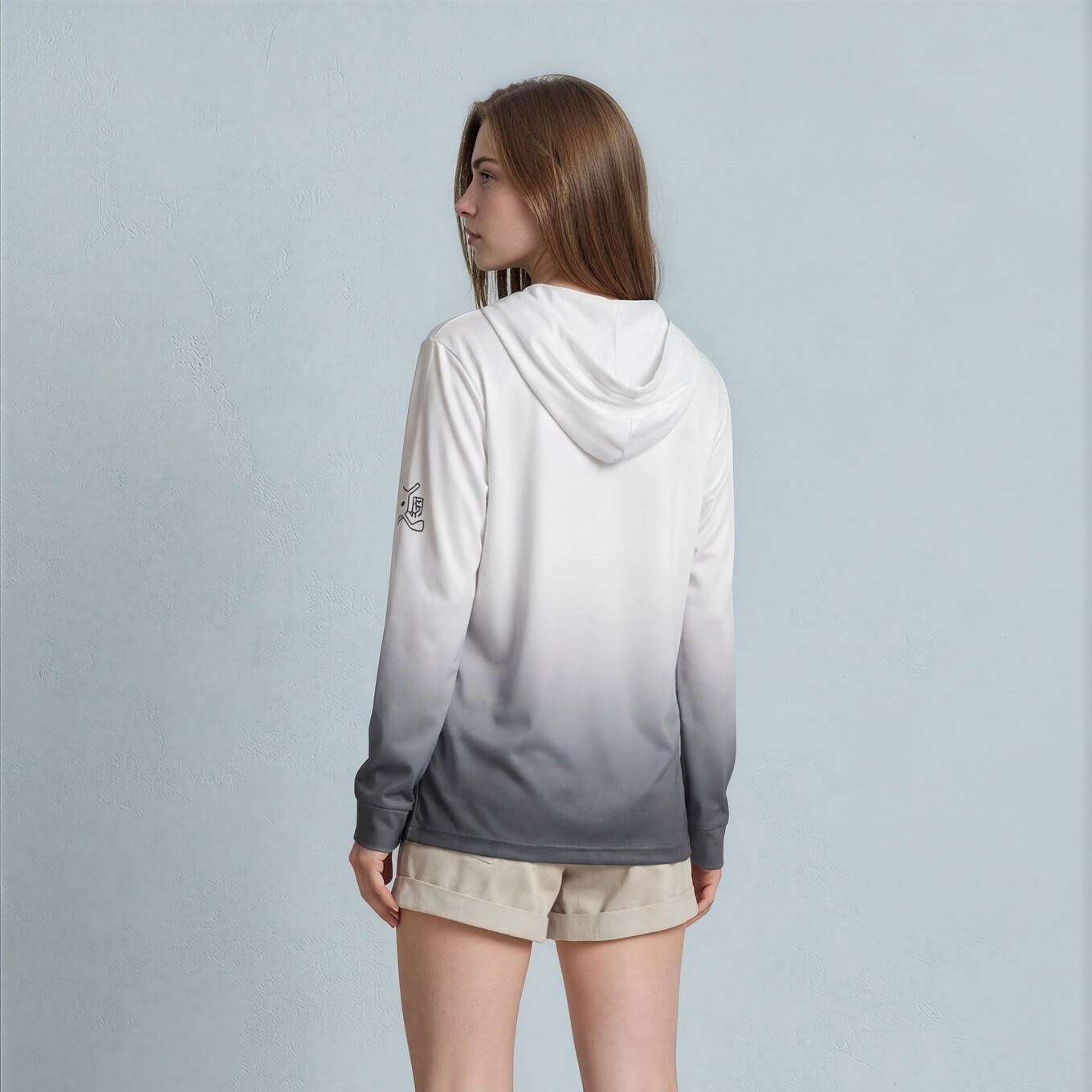 Woman wearing a gray gradient hoodie and beige shorts against a light blue background