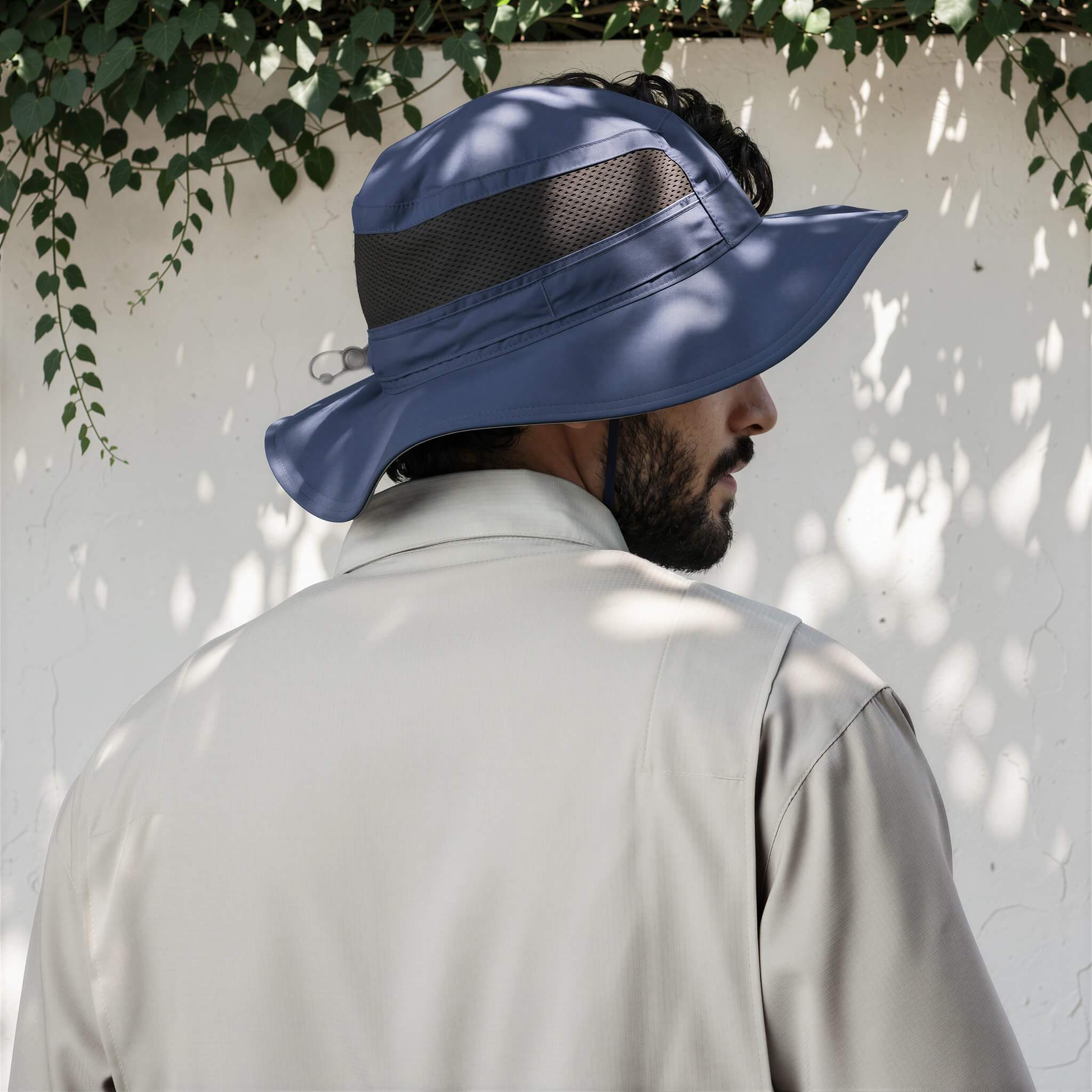 Person wearing a blue bucket hat against a white wall with greenery.
