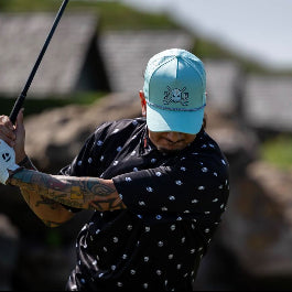Person in a polka dot shirt and blue cap swinging a golf club with blurred background